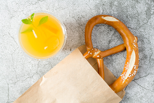 Pretzel wrapped in wrapping paper with drink next to it on stone table