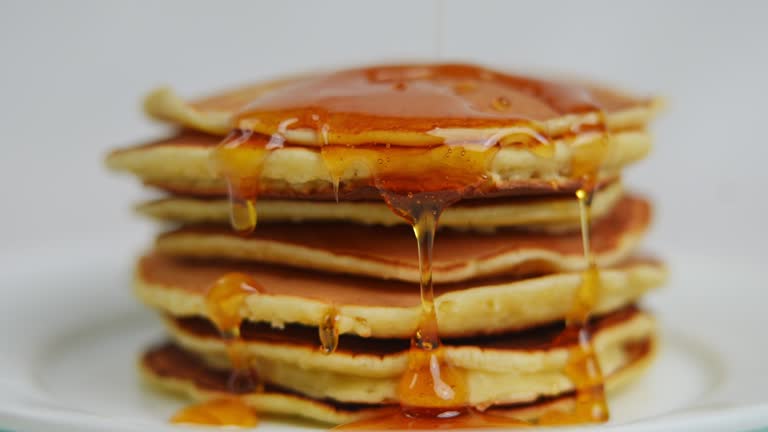 Delicious golden honey flowing on pile of crepes closeup. Close-up tasty sweet dessert food at white background.