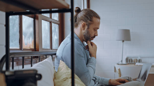 istock Young worried man using laptop sitting on bed at bedroom. 1492544758