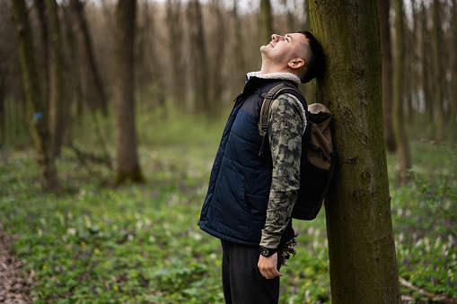 Portrait of man with backpack leaned his back against a tree on forest. Love to nature.
