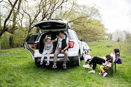 Family with three kids against car open trunk on picnic.