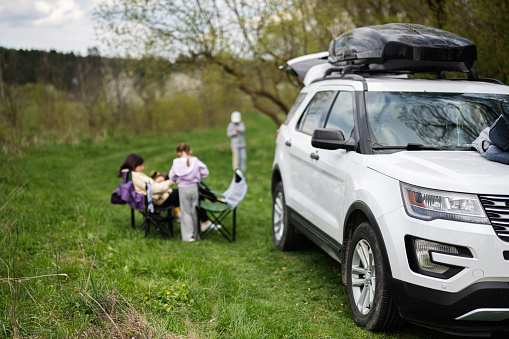 Suv car with roof rack box against family on picnic.