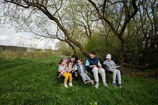 Mother with four kids sitting on chairs at spring forest.