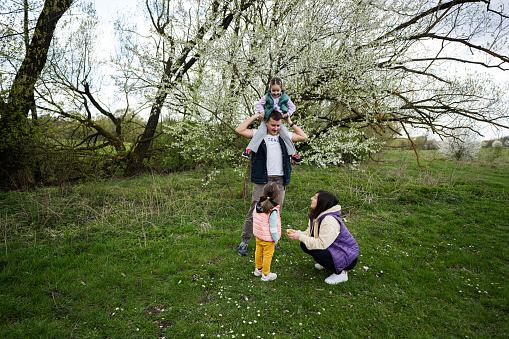 Family with two daughters in spring meadow on the background of a flowering tree.