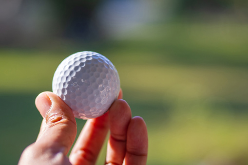 Close-up of female hand holding golf ball with green background.