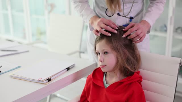 Doctor looks for insects in hair of girl patient in office