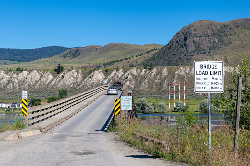 View of wooden Pritchard Bridge (stringer bridge) across South Thompson River, Pritchard, BC, Canada, with in forefront sign with Bridge Load Limit and cars on single lane bridge deck
