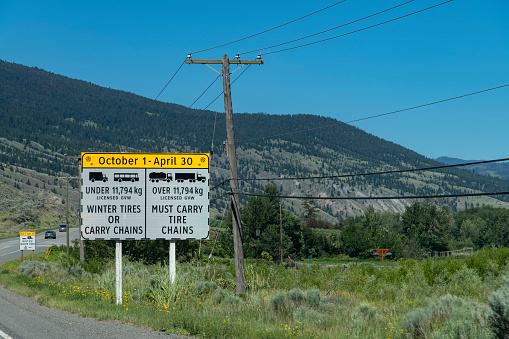 View of a warning sign along the road in the mountainous Kamloops, BC, Canada area, indication need for winter tires of tire chains during certain period of the year