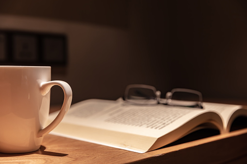 Open book with glasses and white coffee cup on wooden table