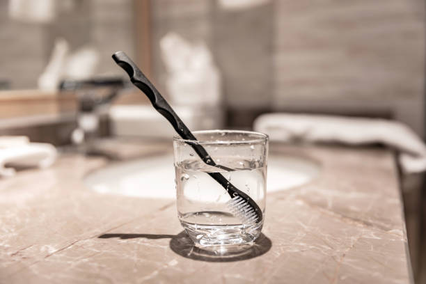 A glass with a toothbrush soaked in it is placed on the sink A glass with a toothbrush soaked in it is placed on the sink 陶瓷器 stock pictures, royalty-free photos & images