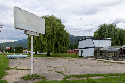 Sicamouse, BC, Canada-August 2022; View of the terrain with signboard and building of a now closed and dilapidated diner with a classic Chrysler New Yorker parked in front