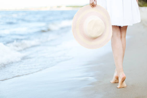 istock Young woman on a beach holding a white hat. Legs close up 1492554151