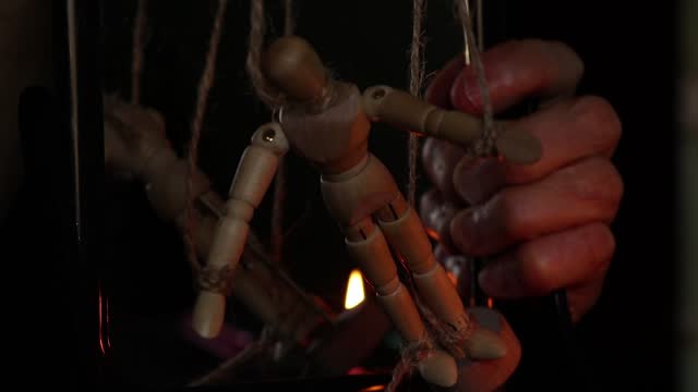 a wooden man on ropes tied to a man's hand, manipulation of people and slavery, free will, power over people
