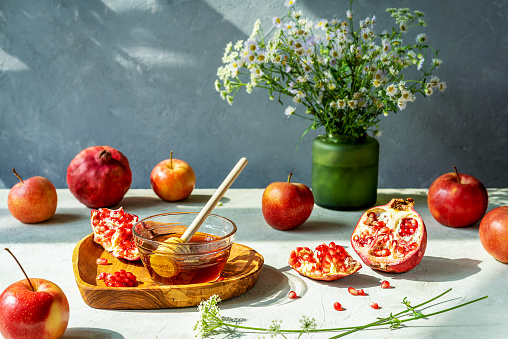 Pomegranates, apples and honey. Rosh Hashanah celebration and autumn harvesting concept. Concrete grey background, wild flowers. Selective focus