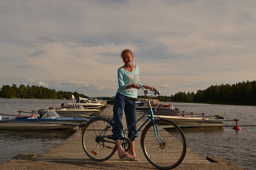 woman stands next to a bike on a dock with boats in the background