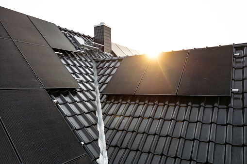 Black solar panels on a dark tiled roof captured with a lens flare at sunrise
