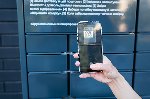 A woman picks up a parcel from a post office by scanning a QR code, online ordering, online shopping. Mail without an employee. Online sales concept