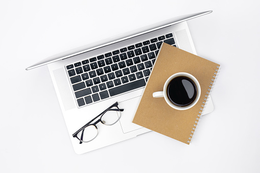 Flat lay white background with laptop, craft notebook, coffee cup and glasses. Work office concept, creative minimalism.