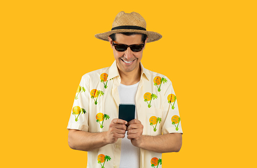 Latin man texting using smartphone over isolated yellow background with a happy face standing and smiling with a confident smile showing teeth