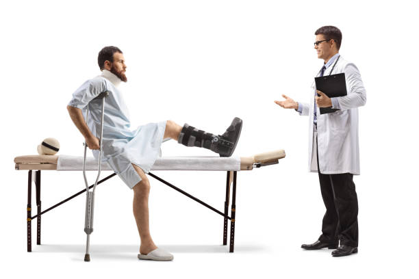 injured man with an orthopedic boot and neck collar sitting on a therapy table and having conversation with a doctor - physical injury men orthopedic equipment isolated on white imagens e fotografias de stock