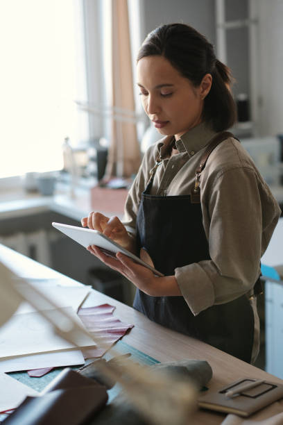 istock Young serious female artisan in workwear scrolling in tablet by workplace 1492560233