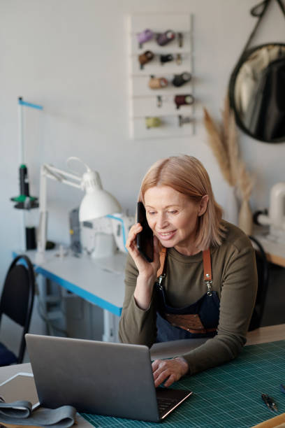 istock Mature smiling female tailor or leatherworker specifying details of online order 1492560499