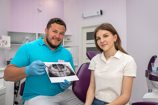 Dentist with hand pointing to x-ray image and talking to female patient about medication and surgical treatment. dental health. treatment of the oral cavity