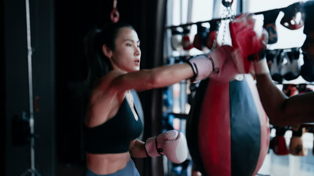 Asian young adult woman in sportswear is doing boxing exercises with a boxing trainer at the gym.