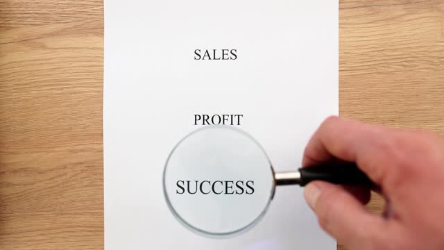Manager points magnifying glass to sales profit and success words