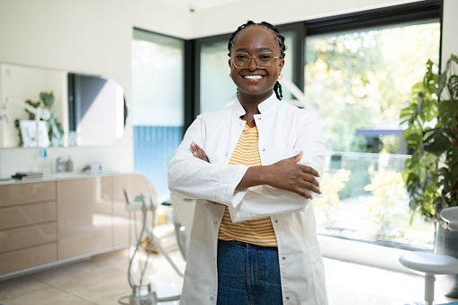 Portrait of happy black orthodontist standing with crossed arms in medical clinic and looking at camera.