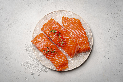 Food background, sliced portions large salmon fillet steaks on chopping board on dark blue concrete table, copy space, top view.