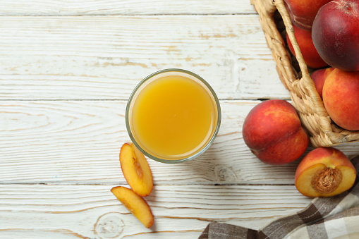 Glass of peach juice and peach fruits on white wooden table
