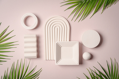 Decorative plaster podiums with palm leaves on pastel pink background, top view, flat lay. Place for product presentation. Creative product platform