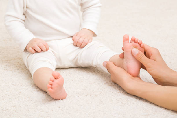 Masseur hand holding infant leg and massaging foot on carpet. Baby healthcare. Closeup. Front view. stock photo