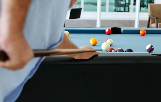 A man strikes a cue on multi-colored billiard balls