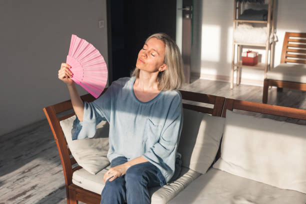 istock Exhausted middle aged woman using paper waver, suffering from hot summer 1492571264