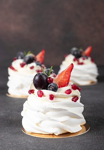 Mini Pavlova cake with strawberry, blueberry, pomegranate and grapes on brown background, vertical format