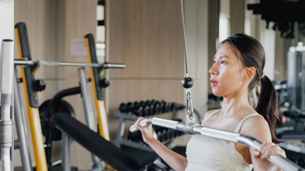 Young Asian athletic sports woman exercise bodybuilder pull-ups on a machine actively training in modern gym. Sports people workout.