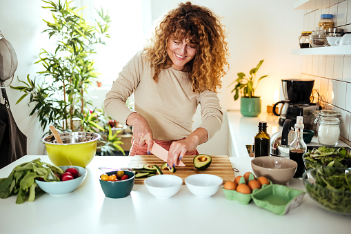 Woman cutting avocado on cutting board to prepare breakfast