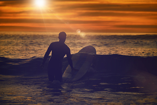 Sports, man and surfer with sunset, fitness and balance with healthy lifestyle, stress relief and relax. Surfboard, male person or guy training, workout and exercise for wellness, waves and adventure