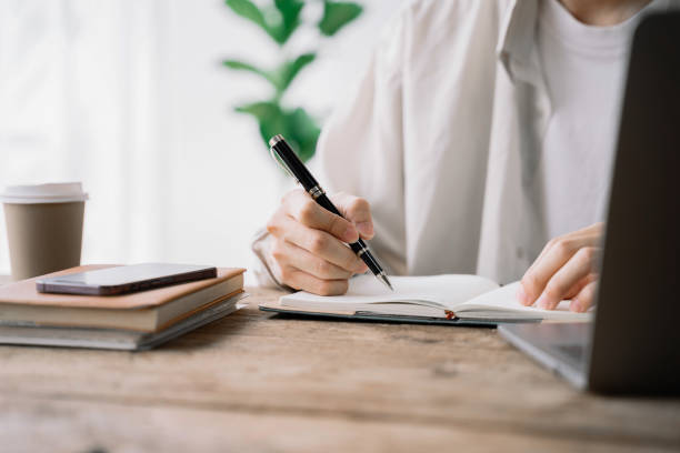 istock Male sitting at a table at home working on a laptop and writing down ideas in a notebook. 1492582199