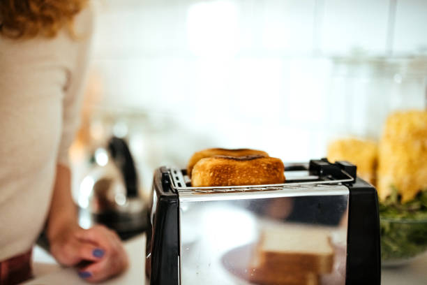 Smiling young woman making breakfast toast bread with toaster at home kitchen