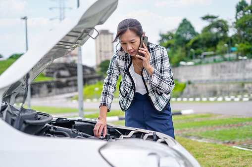 woman in business wear checking car engine while calling assistance after car breakdown at roadside