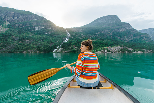 Scenic  view of woman in colourful sweater canoeing on the lake in Norway
