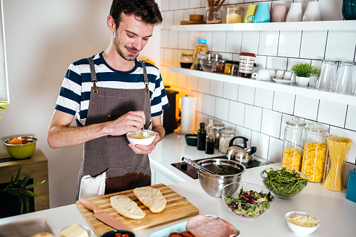 Young man preparing sandwiches at  table in kitchen