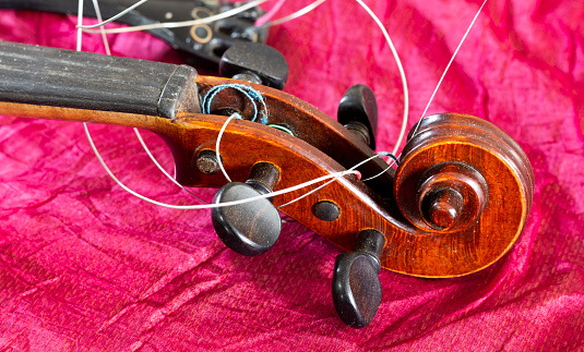 Broken violin and tangled strings, on a red background.