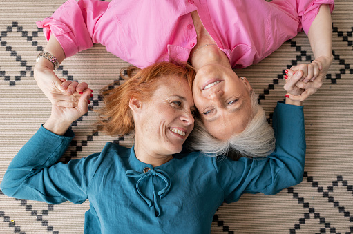 two mature women lying upside down on carpet looking at camera, smiling lesbian women