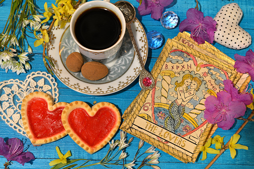 Tarot cards with love symbols, old cup and cookies on witch ritual table. Occult, esoteric and divination still life. Mystic background with vintage objects
