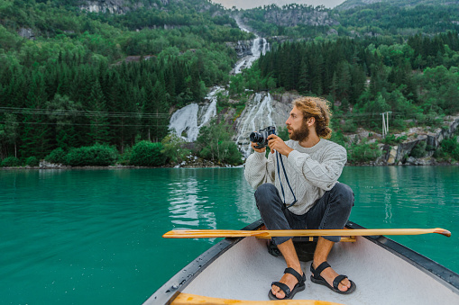 Young man photographing while canoeing on the lake in Norway
