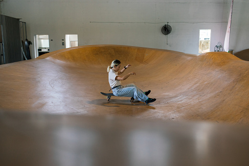 Woman sits on a skateboard in a skating bowl attempting to skate